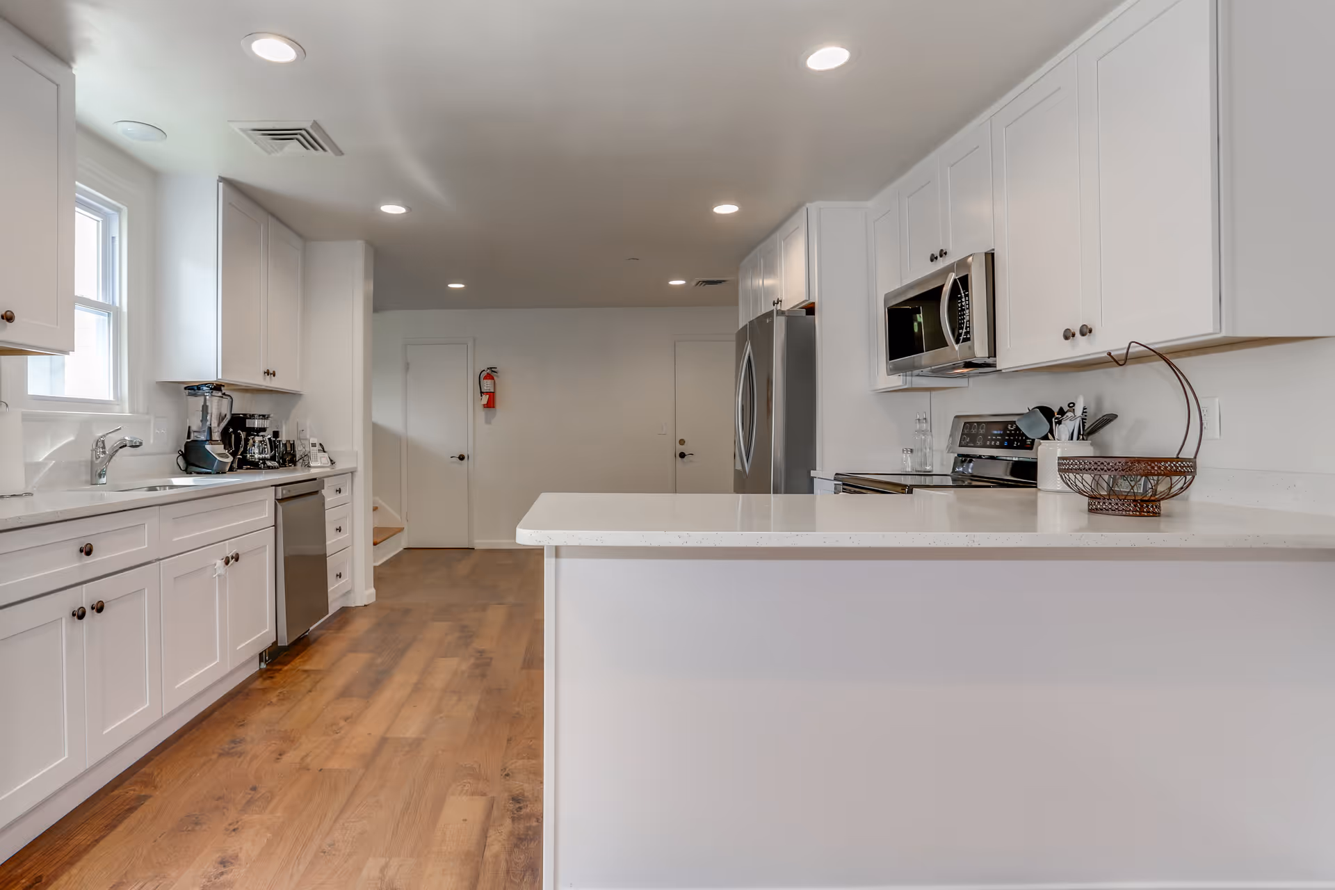 Bright modern kitchen with white cabinets, a large island countertop, stainless steel appliances, and wood floors.