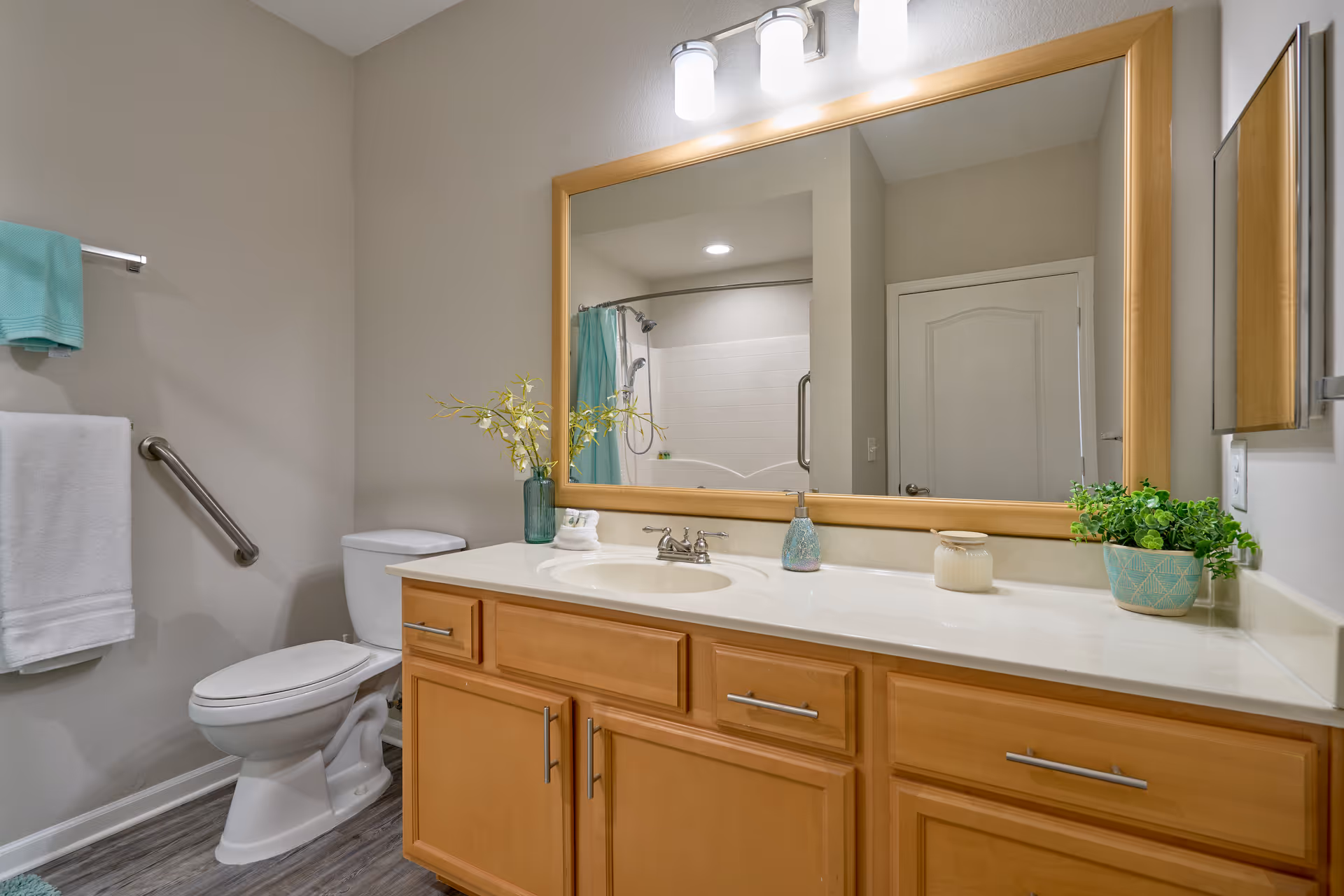 Bright bathroom with a wooden vanity, large mirror, sink, toilet and towel rack.