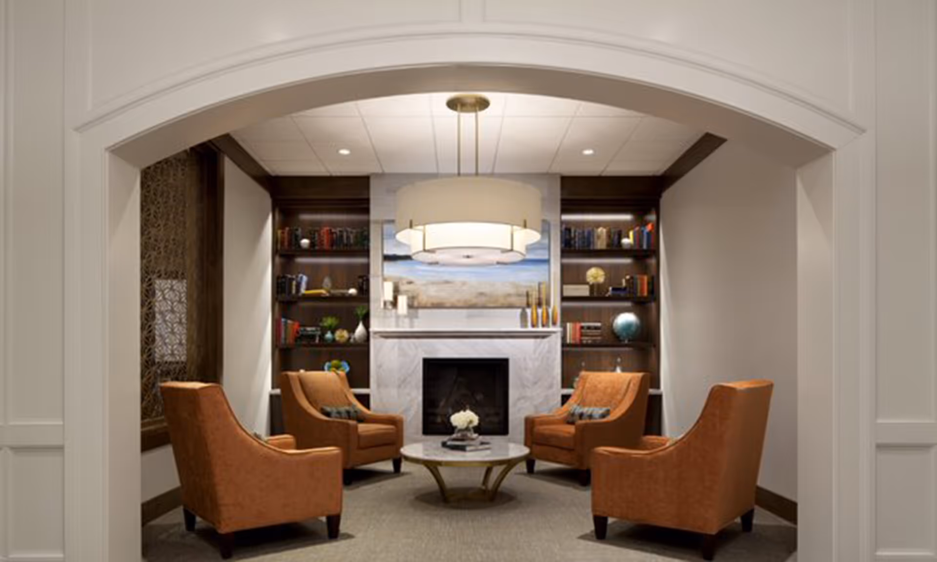 Cozy sitting area with four orange armchairs arranged around a round coffee table in front of a fireplace and built-in bookshelves.