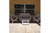 Outdoor patio with white wicker chairs around a small table in front of a windowed wall