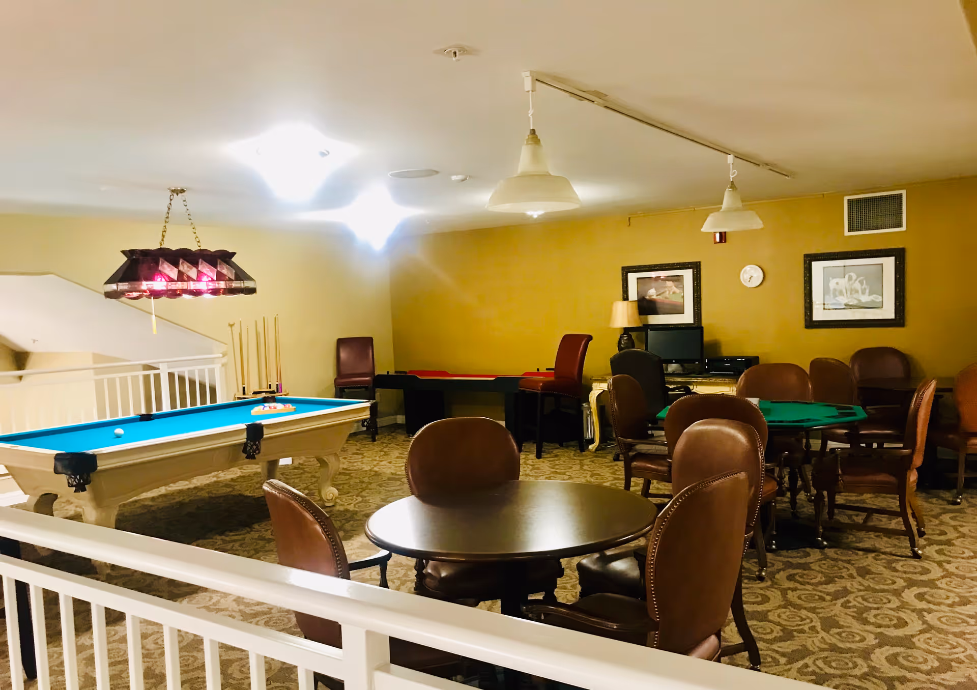 A recreation room with a pool table, card tables, and multiple leather chairs in a furnished common area.
