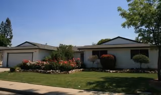 Front view of a single-story care home with lawn, shrubs, and blooming flowers.