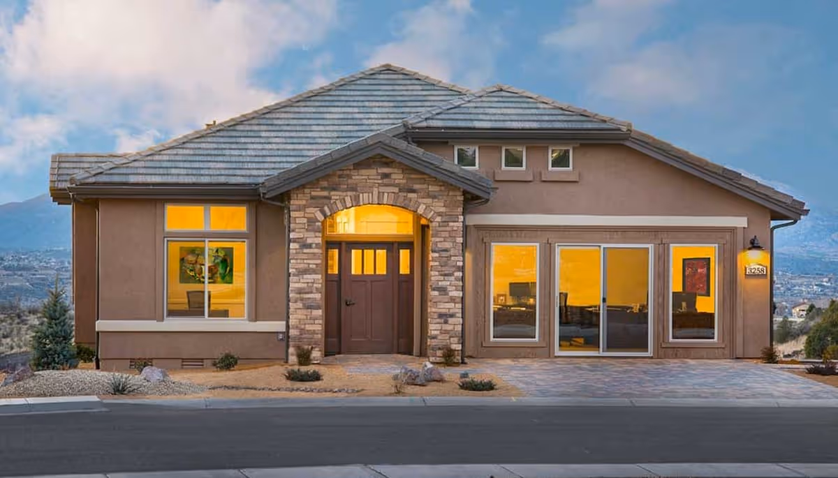 Front exterior view of a single-story house with a stone archway entrance, large windows, and a tiled roof under a partly cloudy sky.