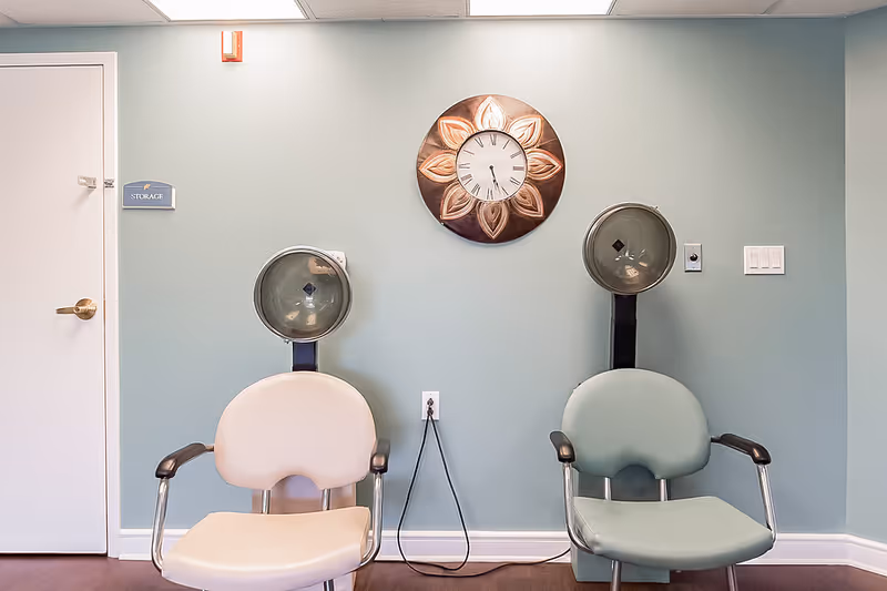 Two salon-style hair dryer chairs against a blue-green wall with a decorative clock and a door labeled 'Storage'.