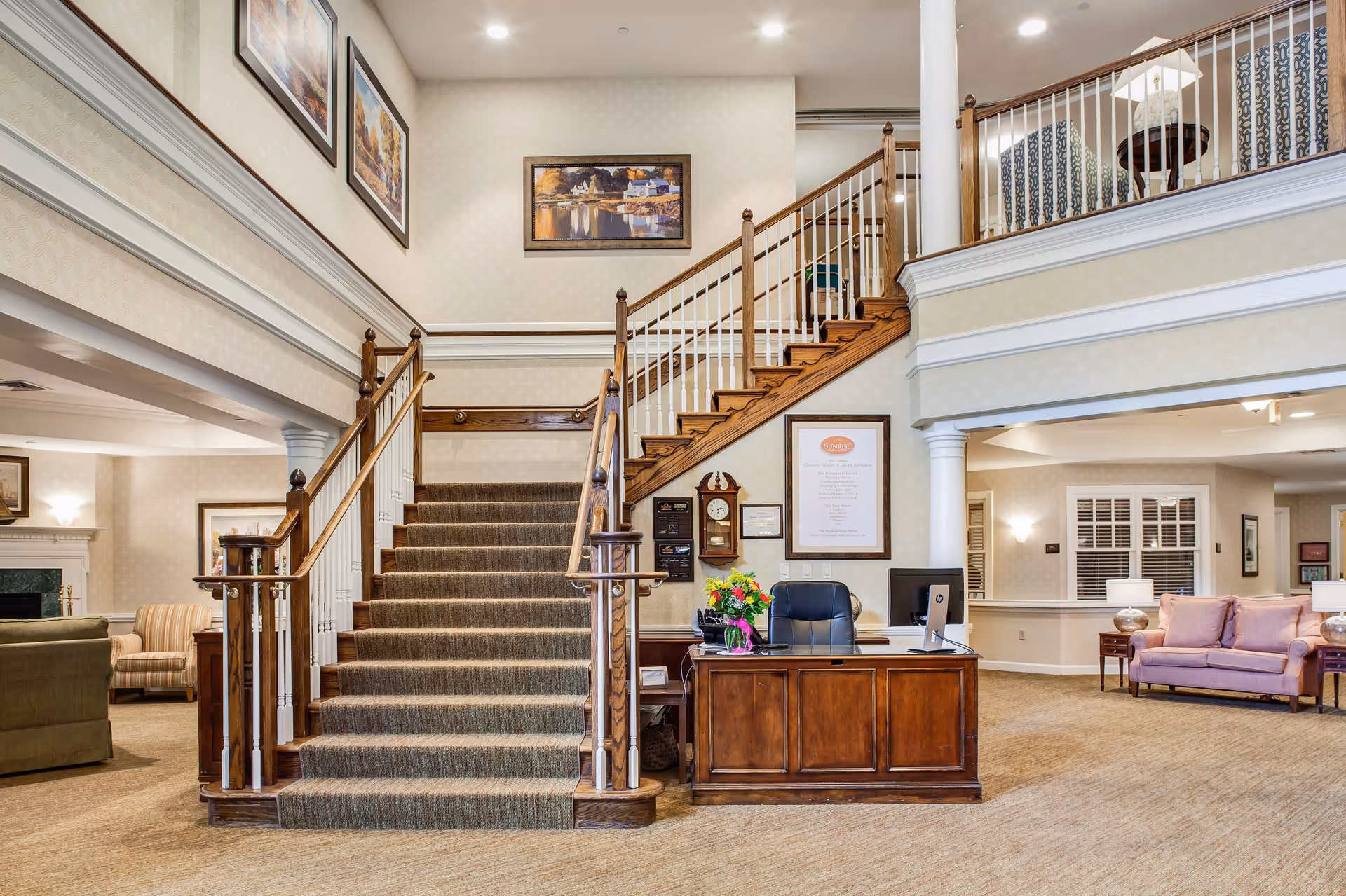 Two-story reception lobby with a central carpeted staircase, wooden reception desk, and seating areas.