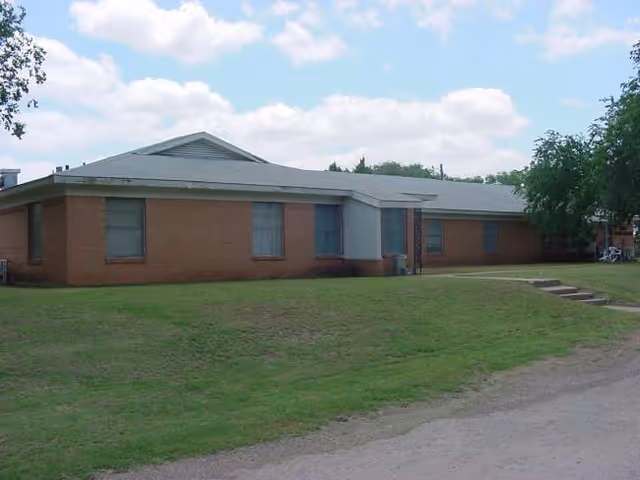 Exterior view of a single-story brick senior living facility with a grassy lawn.
