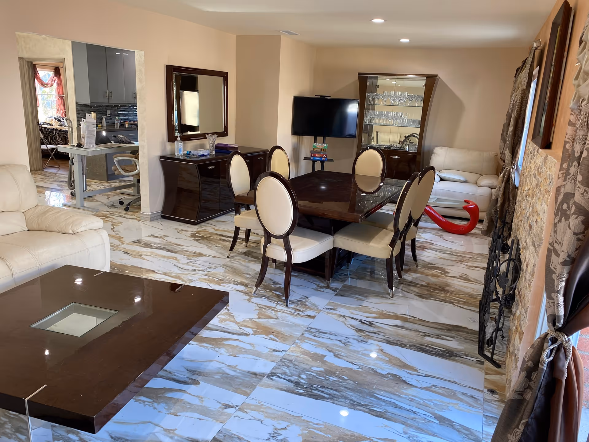 Open living and dining area with marble-look tiled floor, dark wood dining table and chairs, cream leather sofas, TV and display cabinet.