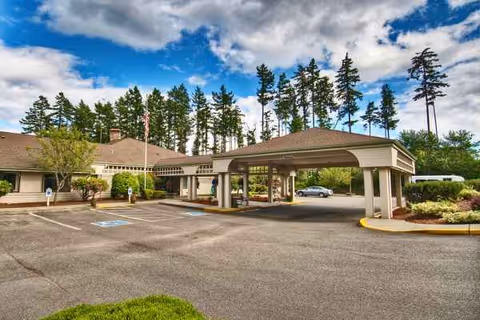 Covered entrance to a senior living facility with parked cars and trees.
