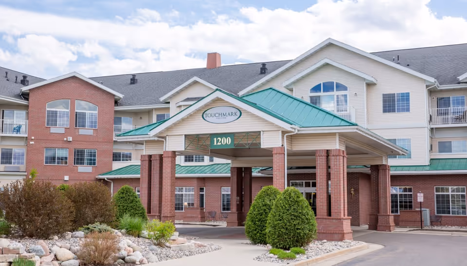 Front entrance of the Touchmark at Harwood Groves senior living building with a covered porte-cochere and green roof displaying the number 1200.