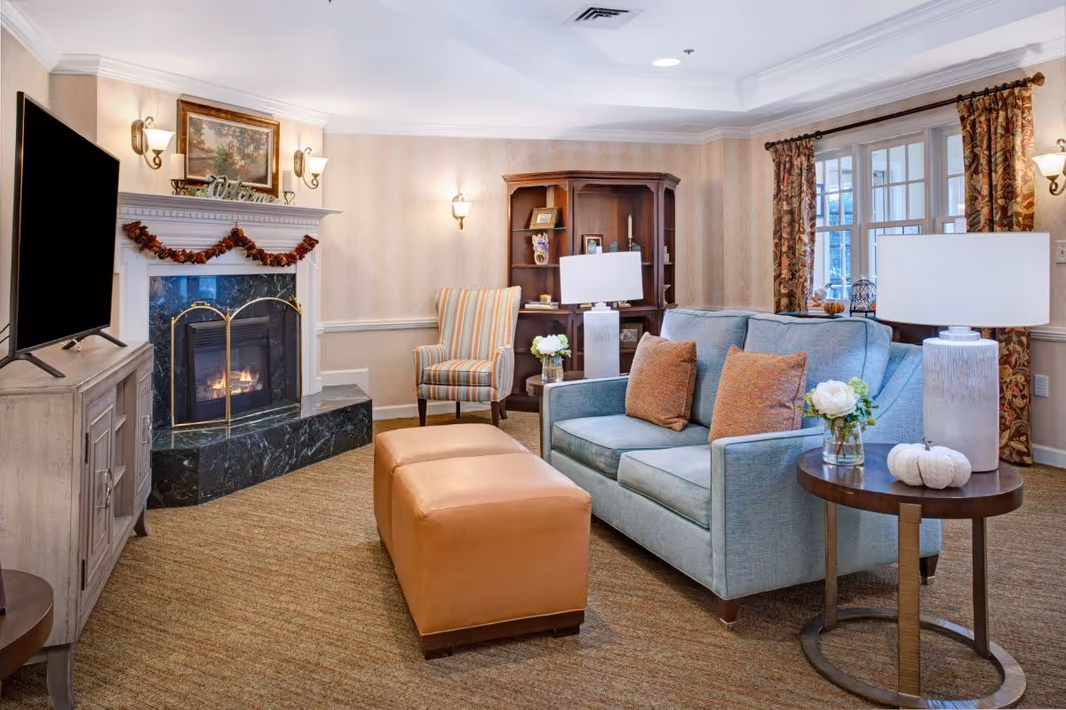 Well-appointed sitting room with a blue sofa, leather ottoman, fireplace, TV, and bookshelves.