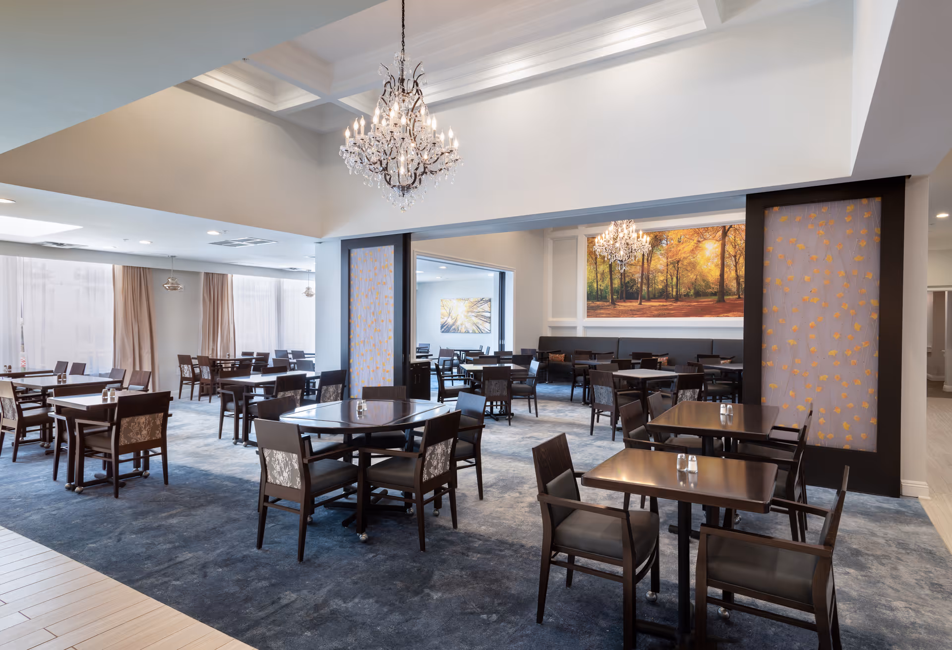 Spacious dining room with multiple wooden tables and chairs, chandeliers, and large wall art.