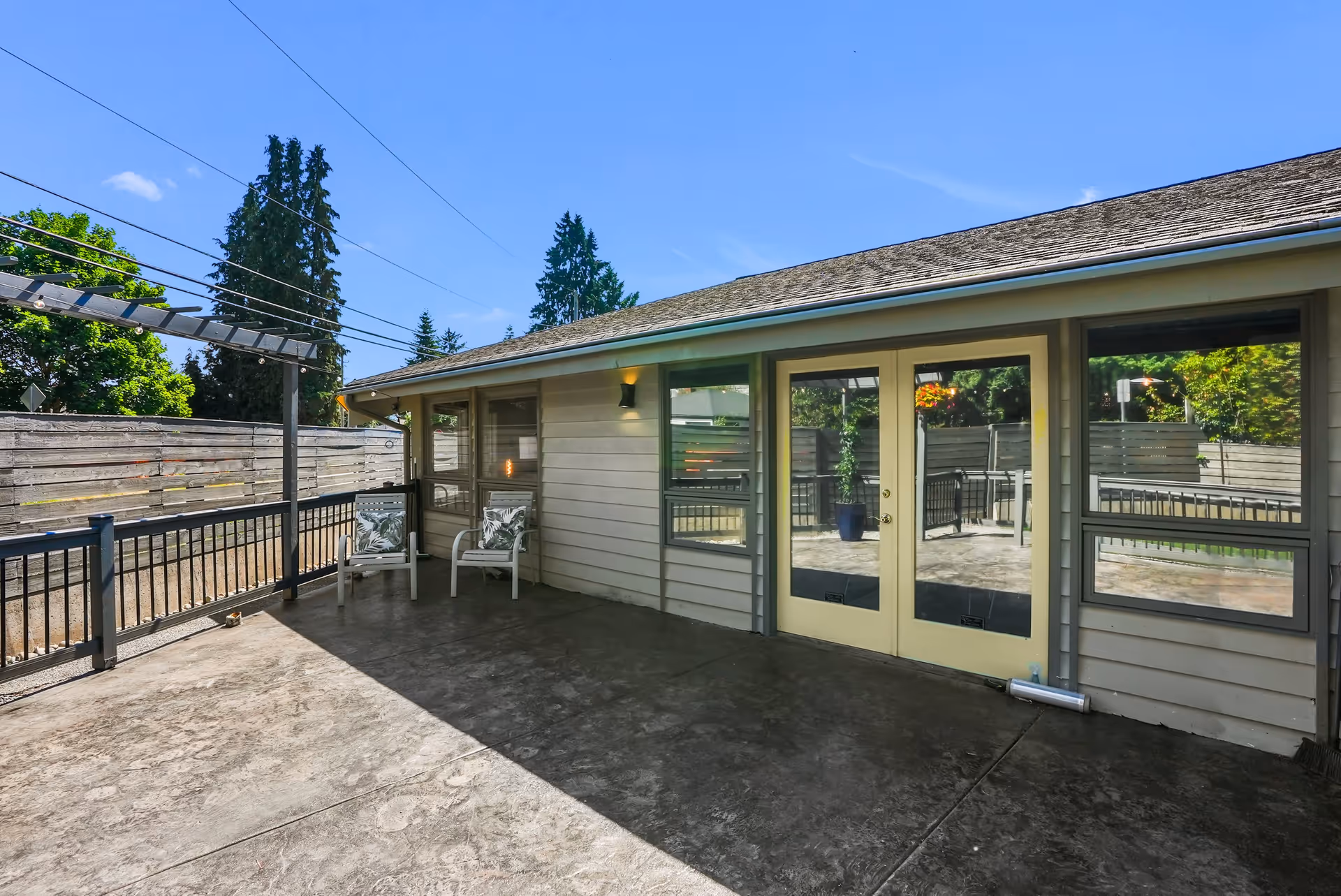 Outdoor patio area of Goodlife Adult Family Home with two chairs, a pergola structure, and a fenced yard under a clear blue sky.