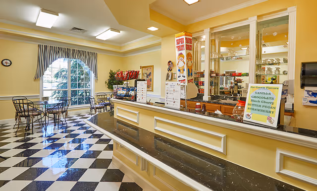 Bright dining and snack area with a black-and-white checkered floor, service counter, and seating by a large window.
