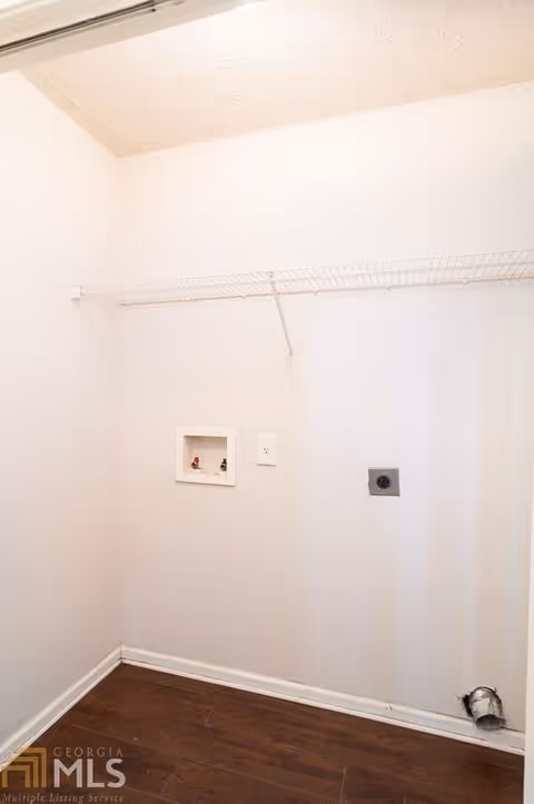 Empty laundry closet with washer/dryer hookups, a wire shelf, and wood-look flooring.