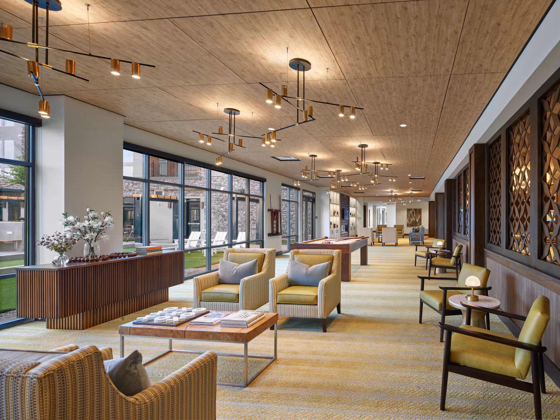 Spacious, contemporary communal lounge with seating areas, a pool table, large floor-to-ceiling windows, and pendant lighting.