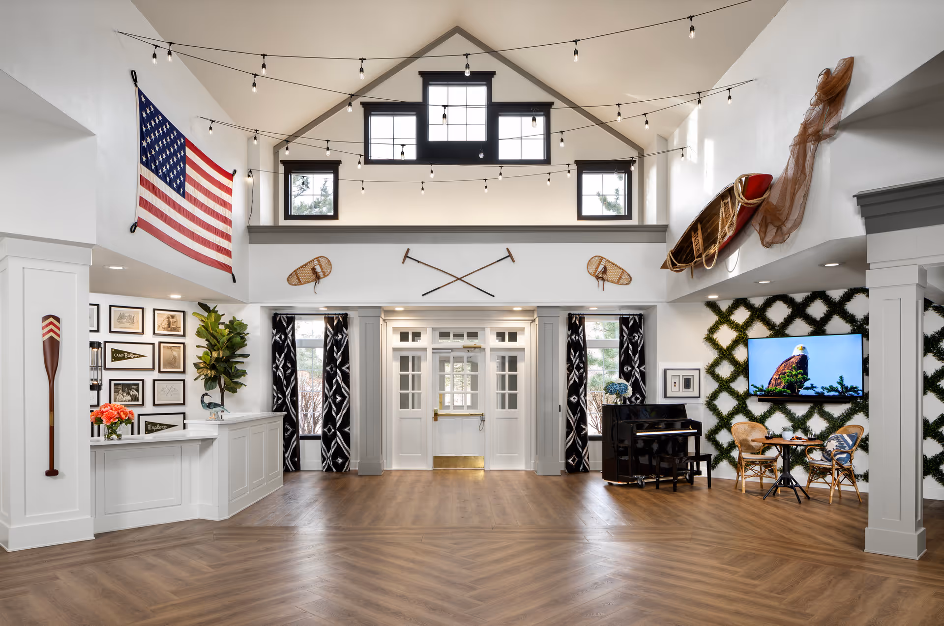 Bright nautical-themed senior living facility lobby with a vaulted ceiling, reception desk, piano, seating area and American flag.