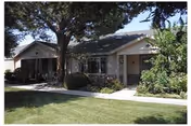 Single-story ranch-style apartment building with a front lawn, walkway, trees, and shrubs.