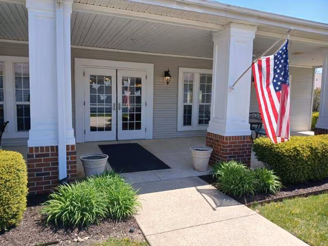 Front entrance of a senior living facility with columns, double doors, and an American flag.