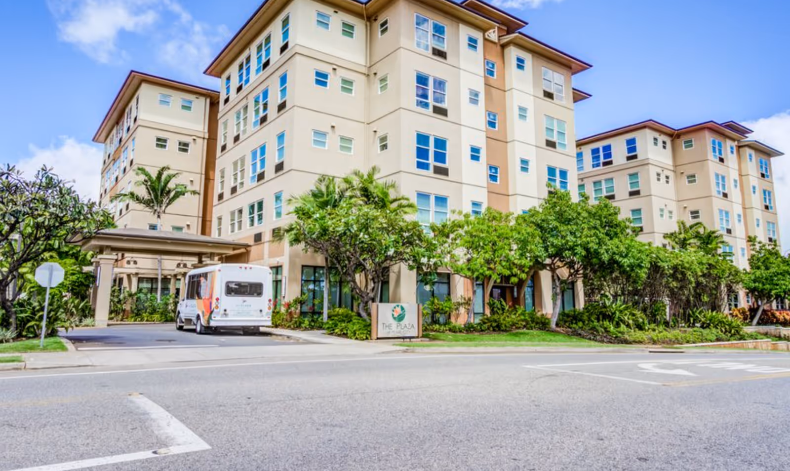Multi-story beige senior living building with landscaped grounds and a shuttle van parked at the covered entrance.