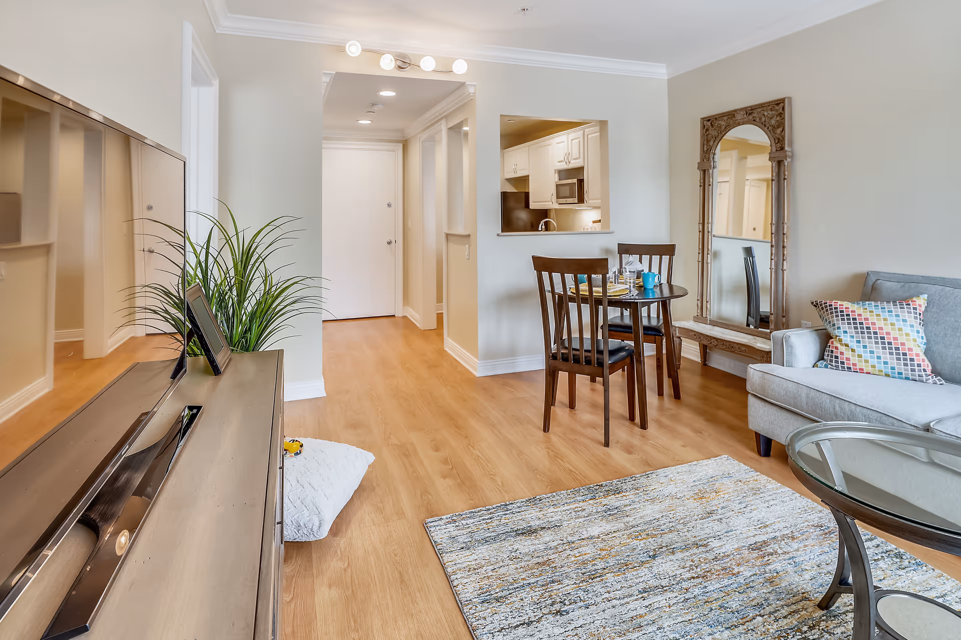 Bright open living area with a sofa, rug, TV console, dining table and a view into the kitchen.