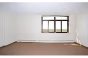 An empty room with a large window, white walls, and a baseboard heater.