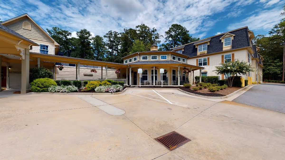 Front exterior of a senior living facility with a covered entrance, circular porch, parking area, and landscaped beds.