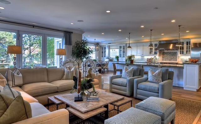Open-plan, well-lit living room with sofas, armchairs and a coffee table opening into a large kitchen with island and pendant lights.