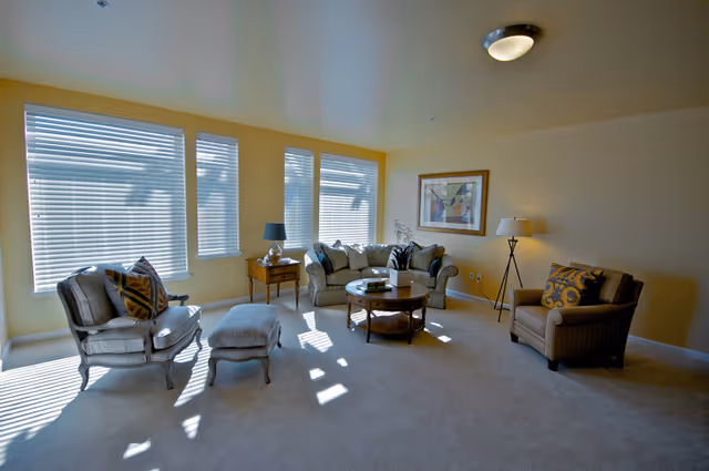 Bright living room with large windows, a sofa and armchairs arranged around a round coffee table and lamps.