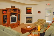 Community living room with sofas, a wooden entertainment center holding a TV, a fireplace, a coffee table, and an exit door.