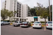 Exterior view of a multi-story residential building with a parking lot and several cars in front.