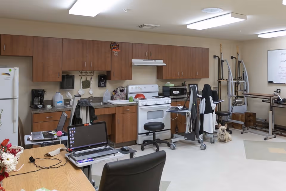 Interior room featuring a kitchenette with wood cabinets and a stove, tables with laptops, and physical therapy equipment.