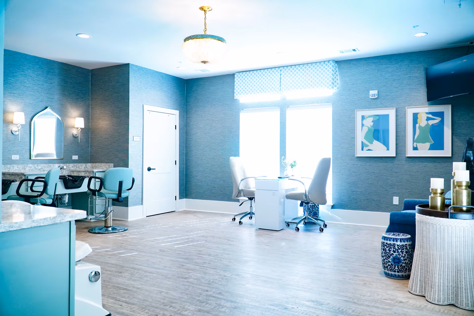 Bright, modern salon-style common room with manicure table, salon chairs, and seating.