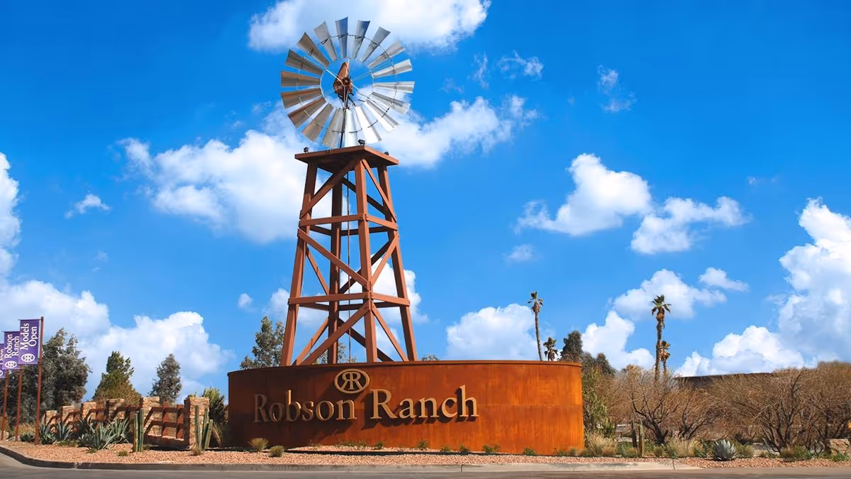 Rust-colored entrance sign reading 'Robson Ranch' topped by a tall windmill tower against a blue sky.