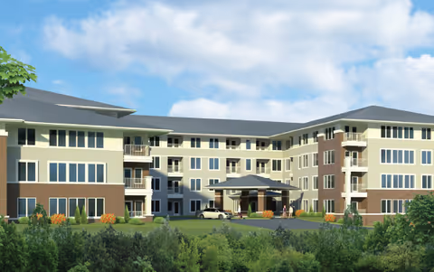 Exterior view of a modern, multi-story senior living facility with a covered entrance, surrounded by greenery and trees under a partly cloudy sky.