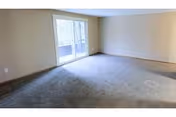 Empty carpeted living room with sliding glass doors opening to a balcony.