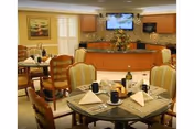 Dining room with several set tables and chairs, a buffet counter with a television and flower arrangement in the background.