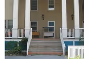 Front entrance of a building with steps, columns, and a porch railing.