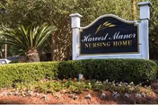 Outdoor view of a sign for Harvest Manor Nursing Home surrounded by neatly trimmed bushes, flowers, and trees in the background.