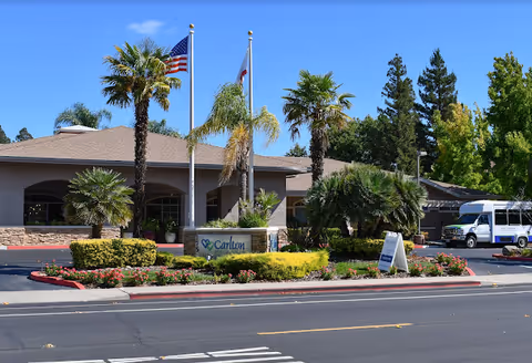Exterior view of Carlton Senior Living Downtown Pleasant Hill entrance with flags and landscaped roundabout.