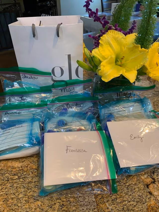 Granite countertop with multiple labeled zip-top bags and envelopes arranged beside a white gift bag and a vase of yellow flowers.