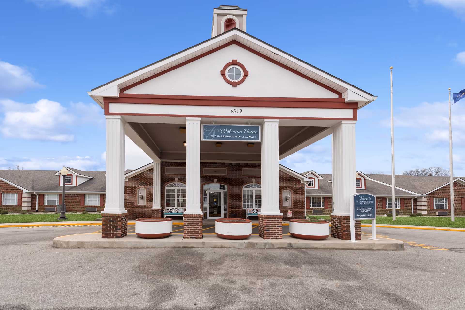 Front entrance of a senior living building with a columned portico, driveway, and signage.
