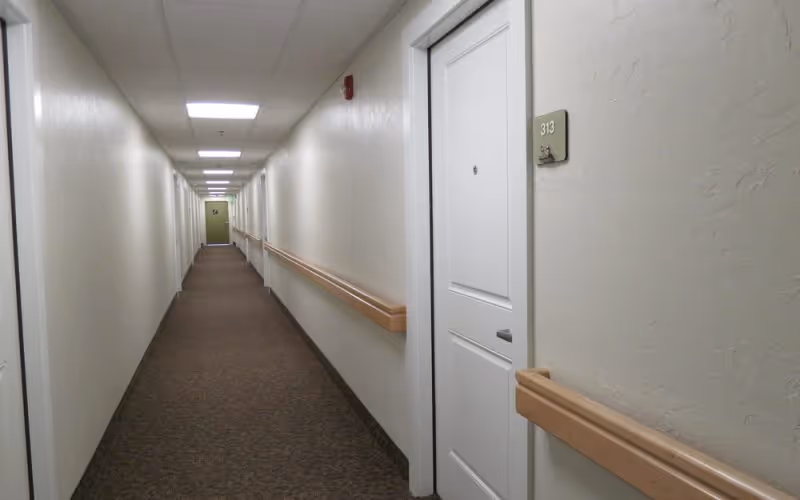 Long, empty hallway in a senior living facility with doors along both walls.