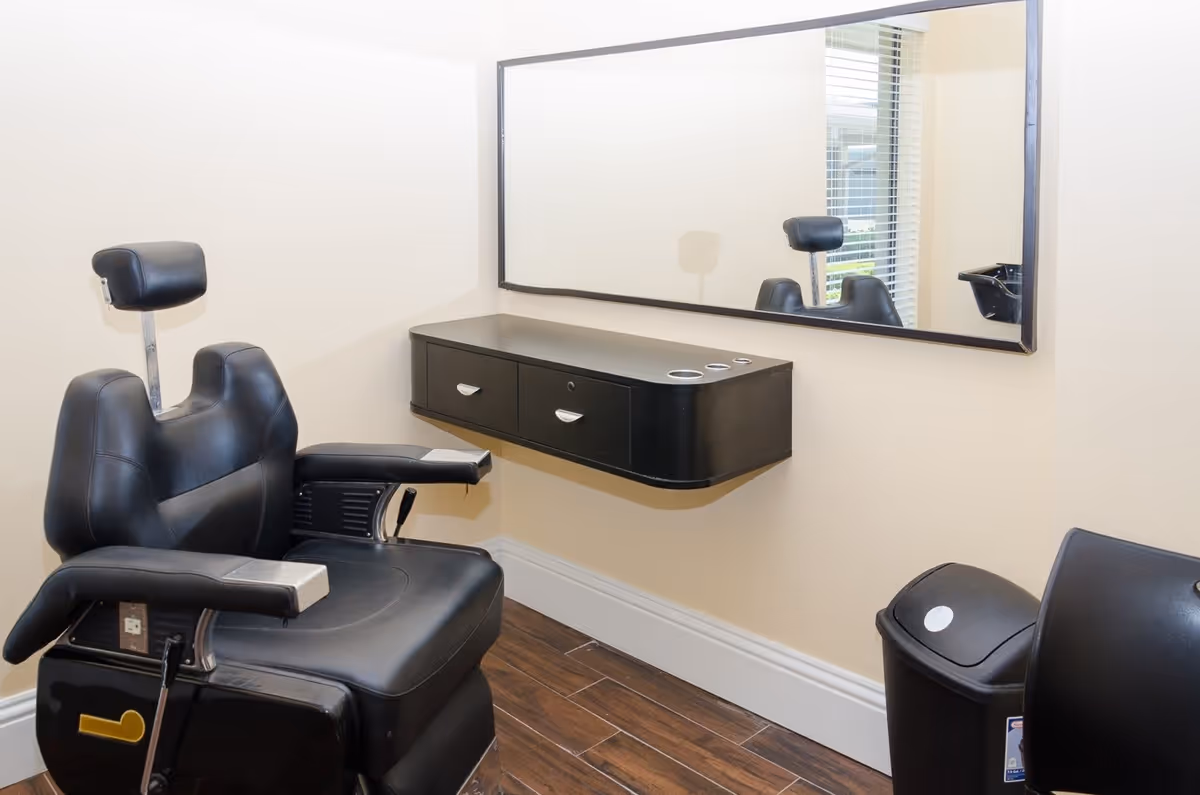 Black barber chair in a small salon room with a wall-mounted vanity drawer and large mirror.