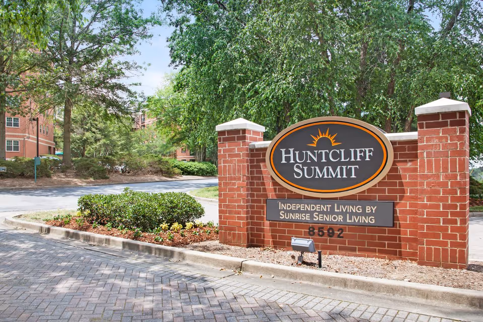 Brick entrance sign reading 'Huntcliff Summit' for a senior living community with landscaping and trees in the background.