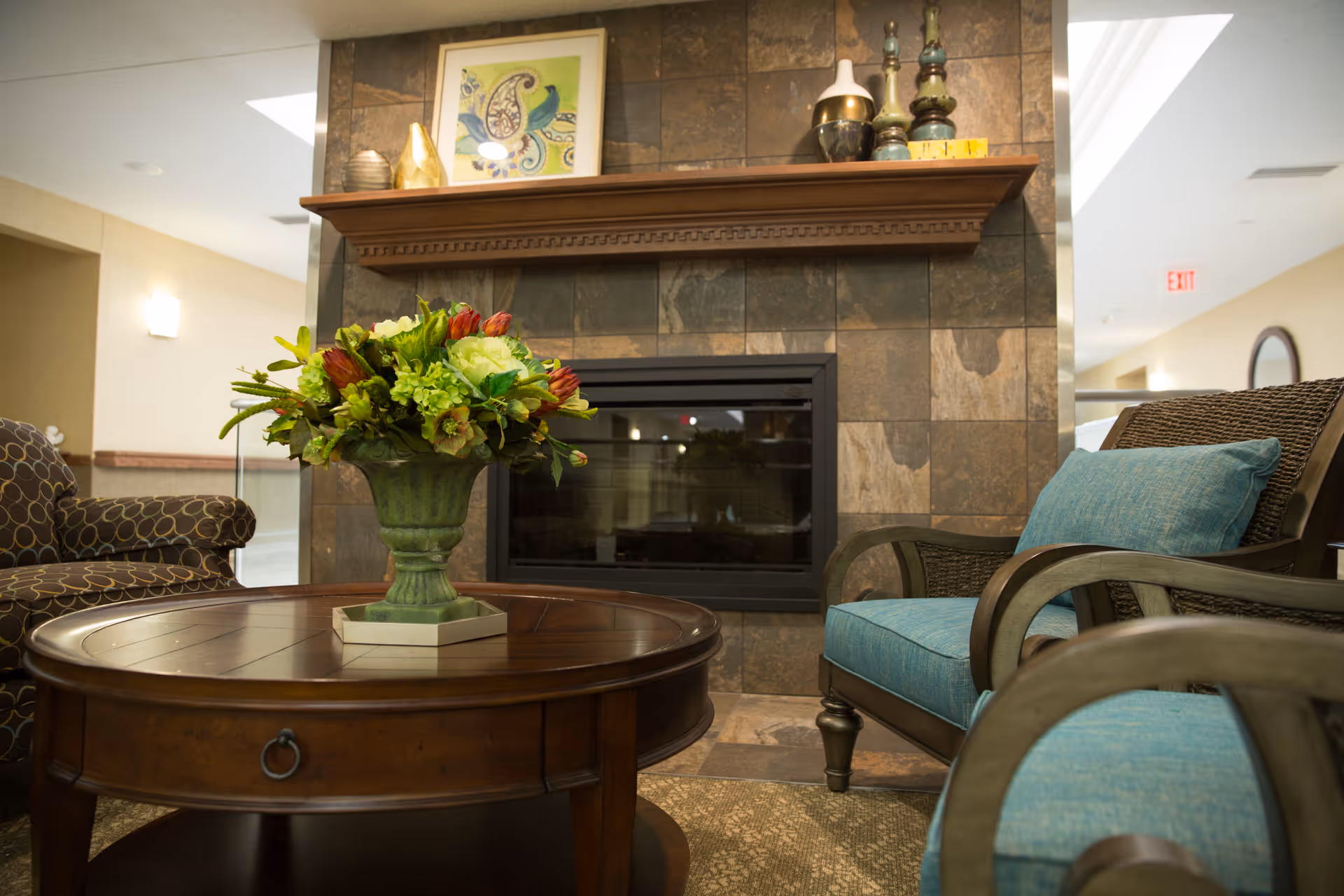 Comfortable seating area with a wooden coffee table topped by a floral arrangement in front of a tiled fireplace.