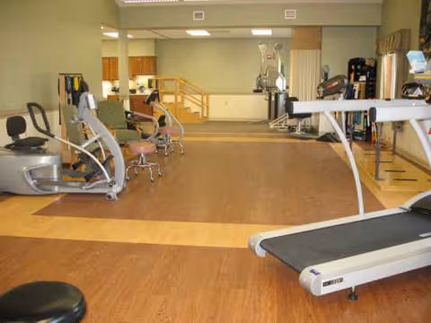 A spacious indoor senior gym with treadmills, exercise machines, and wooden flooring.