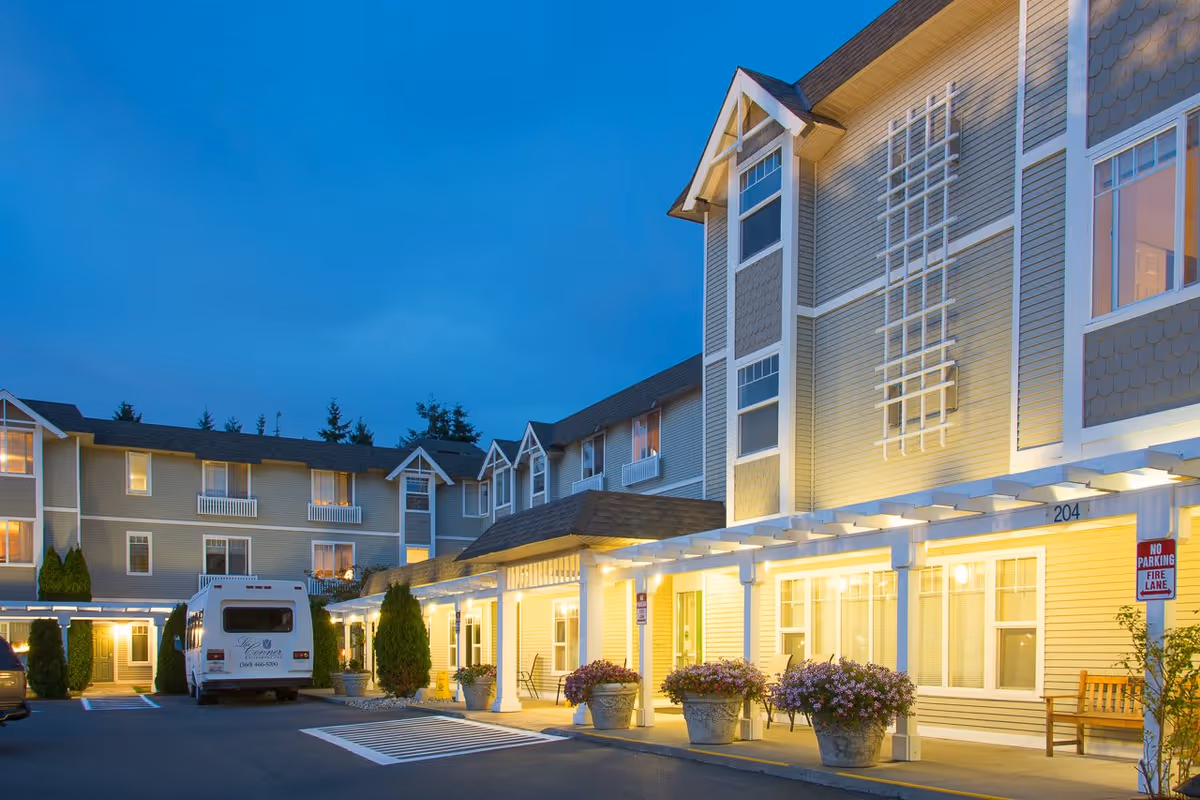 Exterior front entrance of La Conner Retirement Inn at dusk with a lit portico, potted flowers and a parked shuttle van.