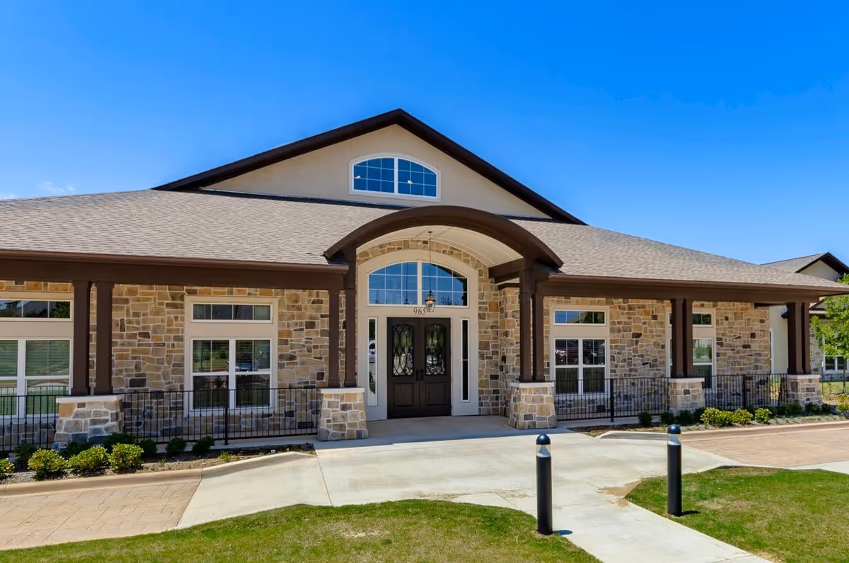 Front view of a stone-clad senior living facility with curved entrance canopy.