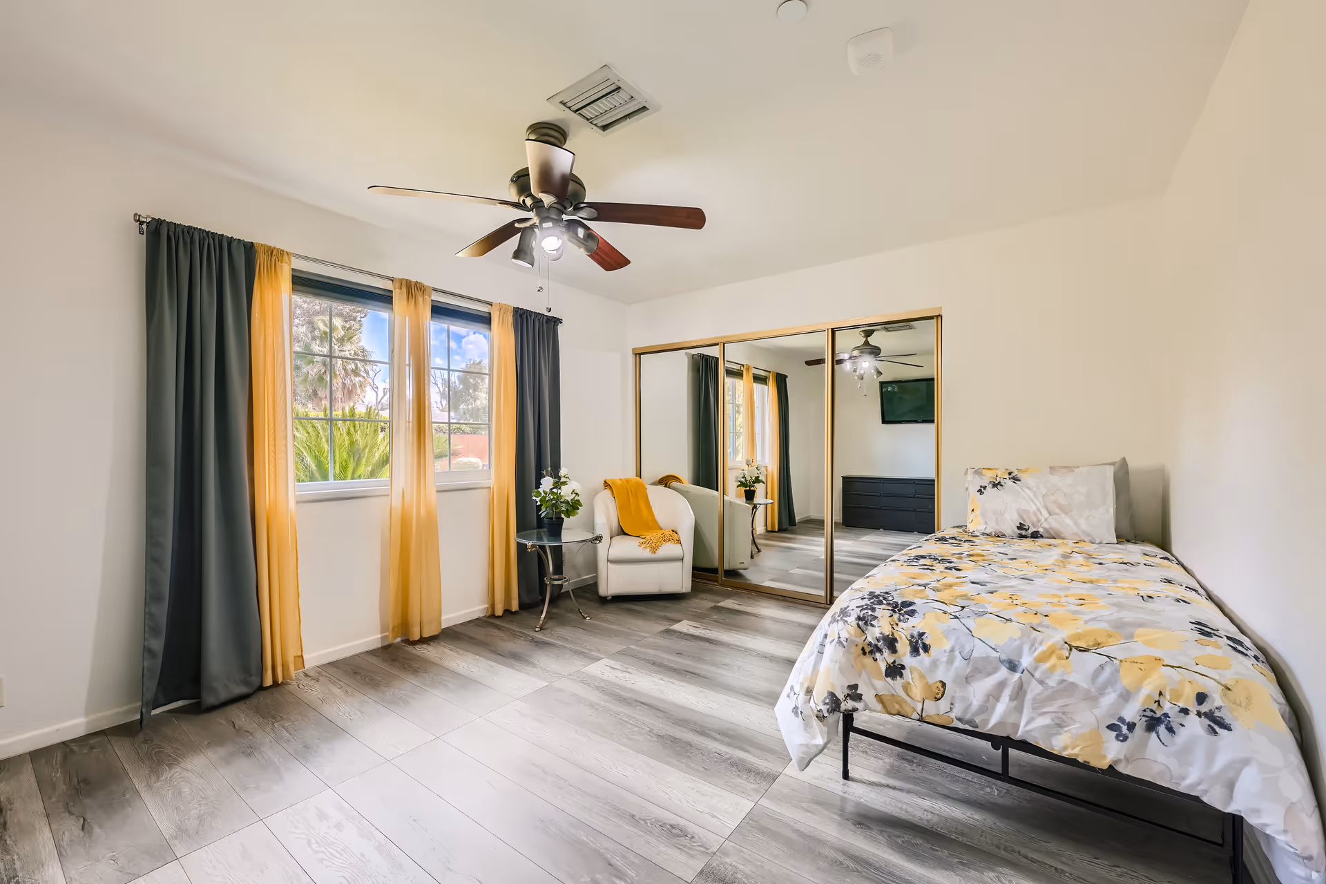 Bright bedroom with a single bed, mirrored closet, armchair and a window with yellow and gray curtains.