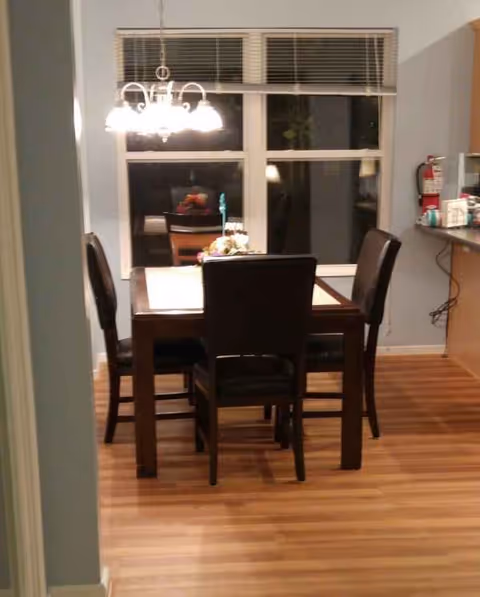 Dining room with a wooden table and four chairs under a chandelier near a large window.
